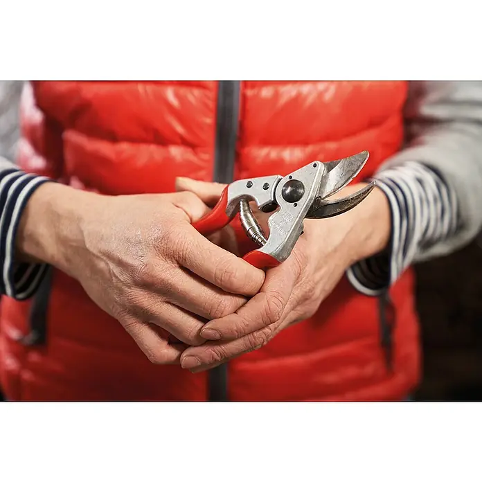 Felco Gartenschere 14 - Bypass, Max. Aststärke: 18 mm - Eine Person hält eine Gartenschere mit roten Griffen vor einer roten Weste. Die Klinge ist leicht abgenutzt und bereit für den Einsatz.