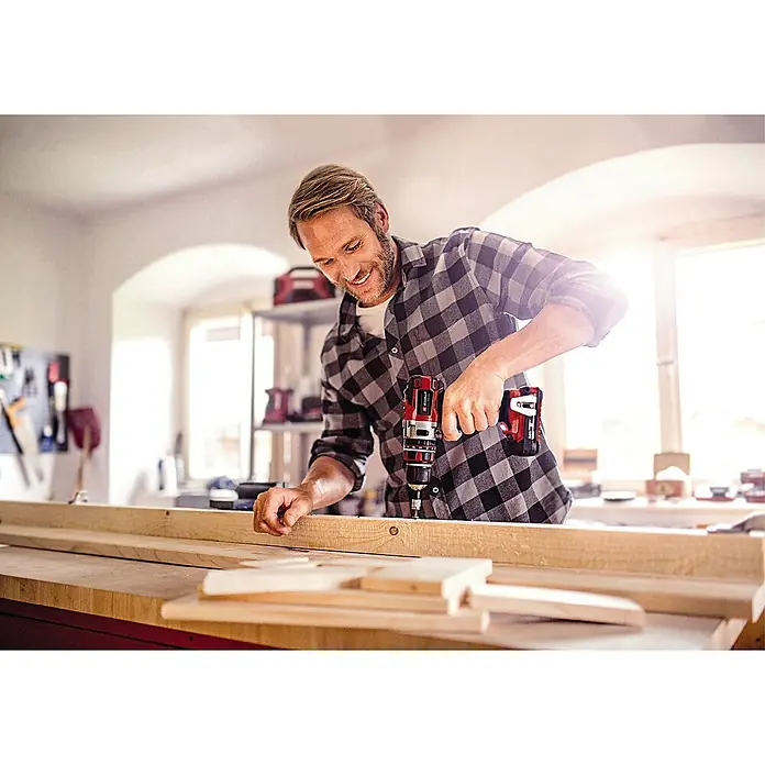 Einhell Professional Power X-Change 18V Akku-Schlagbohrschrauber TE-CD 18 Li-i Brushless-Solo - 18 V, Ohne Akku, 60 Nm - Ein Mann schraubt mit einem roten Einhell Akku-Bohrschrauber in ein Holzbrett in seiner Werkstatt.