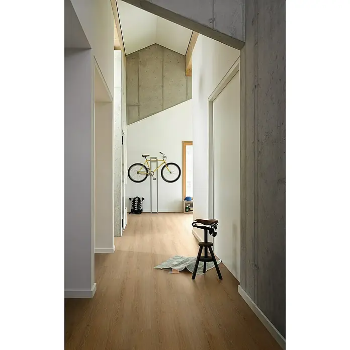 Parador Vinylboden Classic 2030 - Eiche Studioline natur Holzstruktur, Landhausdiele, 1.207 x 216 x 9,6 mm - Innenaufnahme eines hellen Flurs mit einem Fahrradständer und einem gelben Fahrrad, sowie einem Hocker. Der Boden ist hellbraun und es gibt Betonwände.