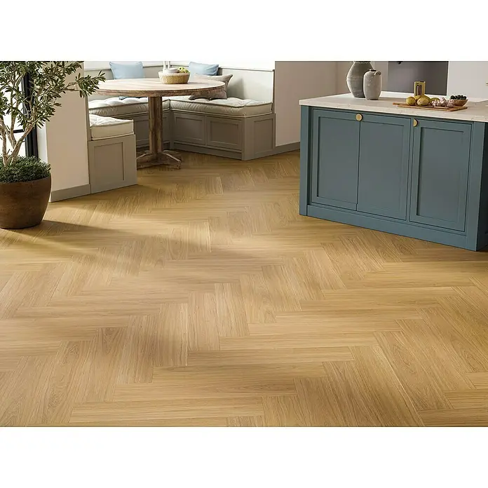 Parador Vinylboden Trendtime 3 - Eiche Oxford karamellbraun, Fischgrät, 730 x 146 x 5 mm - Helles Eichenparkett im Fischgrätmuster mit einem Küchentisch und einer Kücheninsel im Hintergrund.