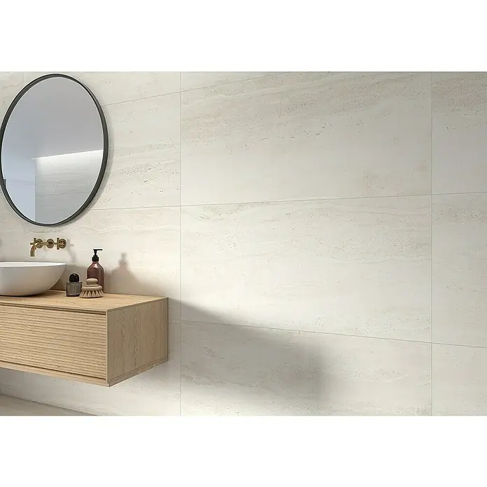 Feinsteinzeugfliese Tivoli 8840 - 60 x 120 cm, Weiß, Matt - Das Bild zeigt ein elegantes Badezimmer mit rechteckigen Wandfliesen in Marmoroptik, einem runden Spiegel und einem Waschtisch mit Holzschubladen.