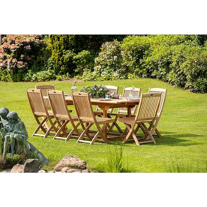 Kai Wiechmann Gartentisch - L x B x H: 120 x 75 x 75 cm, Teak, Rechteckig, Naturbelassen - Eine Gartenszene mit einem hölzernen Esstisch und Stühlen, dekoriert mit Blumen und Geschirr, auf einem gepflegten Rasen mit Büschen im Hintergrund.