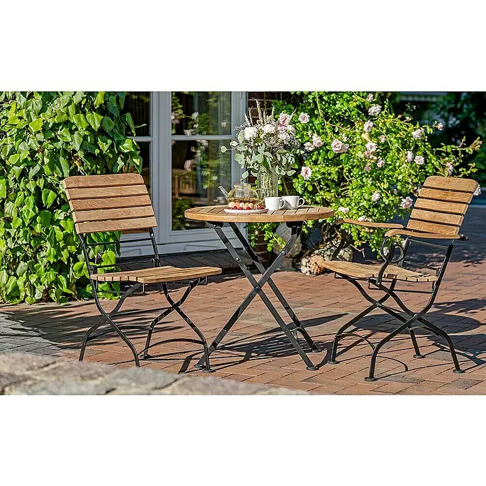 Kai Wiechmann Gartentisch - L x B x H: 70 x 70 x 72 cm, Ø x H: 70 x 72 cm, Teak, Rund, Naturbelassen - Gartensitzgruppe mit Holztisch und zwei Stühlen auf einer Terrasse, umgeben von üppigem Grün, ideal für entspannte Stunden im Freien.