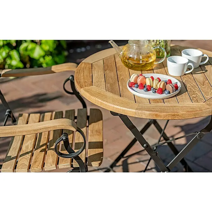 Kai Wiechmann Gartentisch - L x B x H: 70 x 70 x 72 cm, Ø x H: 70 x 72 cm, Teak, Rund, Naturbelassen - Gartenszene mit einem runden Holztisch und Stuhl, dekoriert mit Macarons, Beeren, Tee und Tassen. Das Set verspricht einen gemütlichen Genuss im Freien.