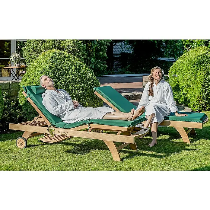 Kai Wiechmann Liegenauflage - Sonnenliege, Hochlehner, Relaxchair, L x B x H: 49 x 36 x 6 cm, Polyacryl, Marineblau - Zwei Personen entspannen sich auf Teakholz-Sonnenliegen mit grünen Auflagen im Garten, ideal für entspannte Stunden im Freien.