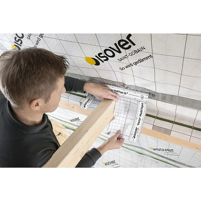 Isover Vario Klebeband Multitape SL+ - 25 m x 60 mm - Ein Mann verwendet ein Isover Vario MultiTape Messwerkzeug, um ein Holzstück zu vermessen, während er an einem Bauprojekt arbeitet.