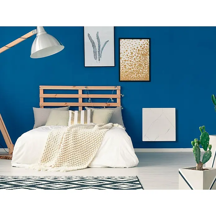 Purline Emisor térmico Marbly A500 - 500 W, Blanco, 7 x 60 x 60 cm - Un dormitorio cuenta con un panel de calefacción blanco marmoleado en una pared azul real, que proporciona calor y un diseño elegante.
