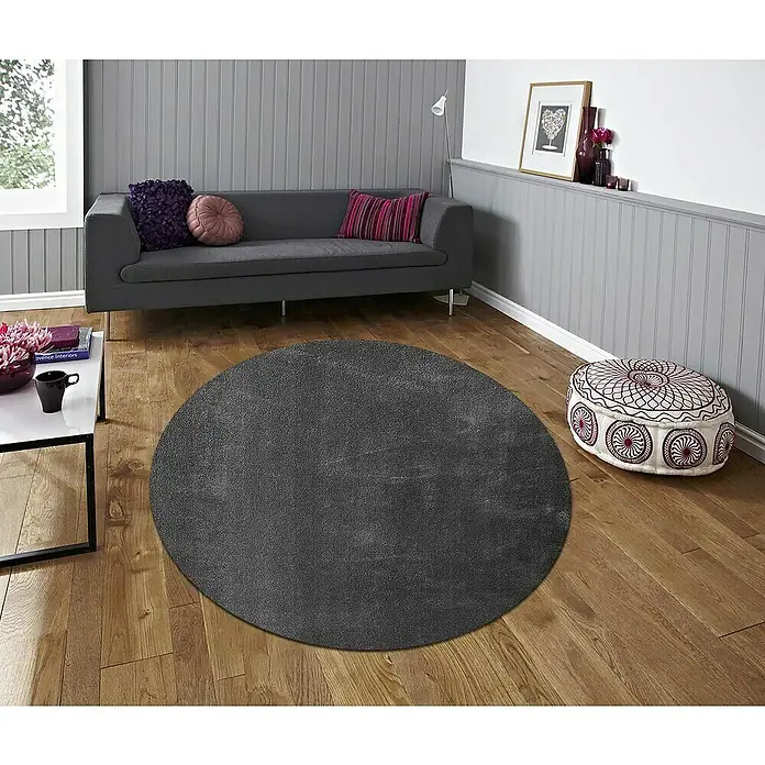 Alfombra de pelo corto Toscana - Gris, Diámetro: 160 cm, 100% Poliéster - Una habitación elegante con una alfombra redonda gris, un sofá gris y un puf estampado, creando un ambiente acogedor y agradable.