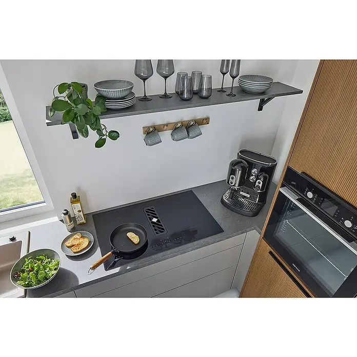 Respekta Induktionskochfeld Calima mit integriertem Dunstabzug - Breite: 83 cm, Schwarz, Max. Gebläseleistung Abluftbetrieb: 544,7 m³/h - Küchenszene mit Induktionskochfeld, Dunstabzugshaube, Espressomaschine, Backofen, Geschirr und Lebensmitteln.