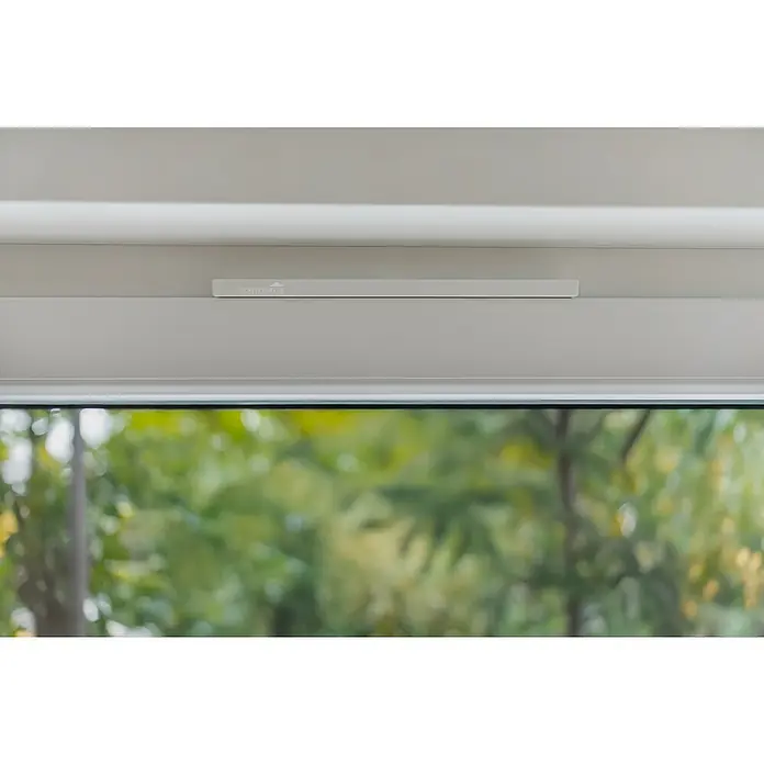 Schellenberg Fensterlüfter Plus Einzelpack - Weiß, 1 Stk. - Nahaufnahme eines Schellenberg-Fenstersensors, der an einem weißen Fensterrahmen befestigt ist, mit Blick auf eine grüne Außenlandschaft.