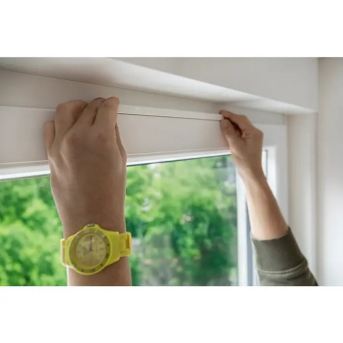 Schellenberg Fensterlüfter Plus Doppelpack - Weiß, 2 Stk. - Eine Person montiert ein neues, weißes Rollo an einem Fensterrahmen. Helle Farben und Tageslicht dominieren das Bild.