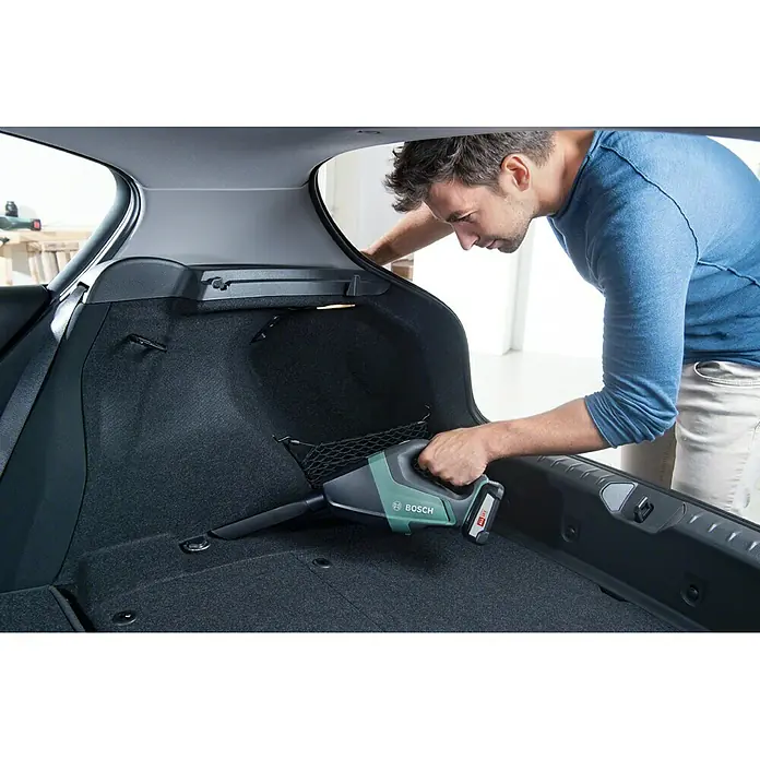 Bosch Power for All 18V Aspirador de mano de batería UniversalVac 18 - 18 V, Sin batería, Volumen de recipiente: 0,5 l - Un hombre limpia el maletero de su coche con una aspiradora de mano inalámbrica Bosch verde, esencial para el cuidado de su coche.
