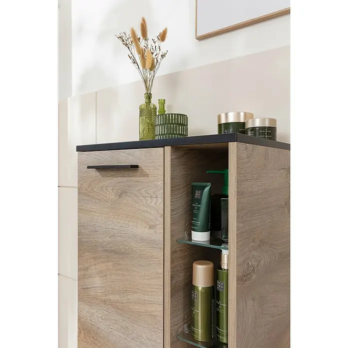 Fackelmann TE-A Midischrank - B x T x H: 47 x 32 x 94,2 cm, Nature Oak Holzoptik - Ein Badezimmerschrank mit Holzstruktur und schwarzen Details bietet Stauraum für Pflegeprodukte wie Cremes und Lotionen, dekoriert mit Vasen und Pflanzen.