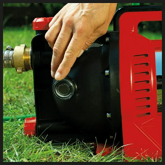 Einhell Gartenpumpe GC-GP 1250 N - Leistung: 1.200 W, Max. Fördermenge: 5.000 l/h - Nahaufnahme einer roten und schwarzen Gartenpumpe mit einer Hand, die einen durchsichtigen Knopf berührt.