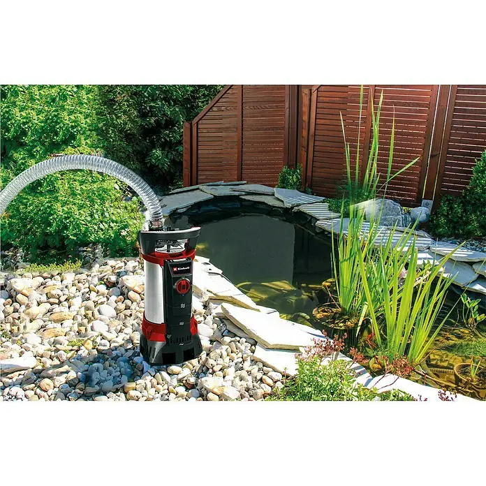 Einhell Schmutzwasserpumpe GE - DP 7935 N-A ECO - 790 kW, Max. Fördermenge: 19.000 l/h, Eintauchtiefe: 7 m - Ein Einhell Schmutzwassertaucher pumpt Wasser aus einem Teich. Die Pumpe ist rot, silber und schwarz und steht auf Steinen.