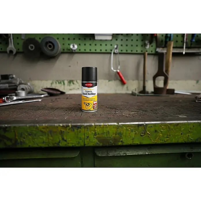 Caramba Rostlöser Express - 100 ml - Die Rostlöser-Sprühdose Caramba Express Schock Rostlöser vor einem Werkstatthintergrund. Ideal für festsitzende Schrauben!
