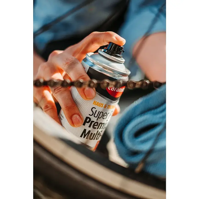 Caramba Multiöl Super Plus Premium - 100 ml - Nahaufnahme einer Person, die Caramba Super Premium Multi-Spray auf eine Fahrradkette sprüht, um Wartungsarbeiten durchzuführen.
