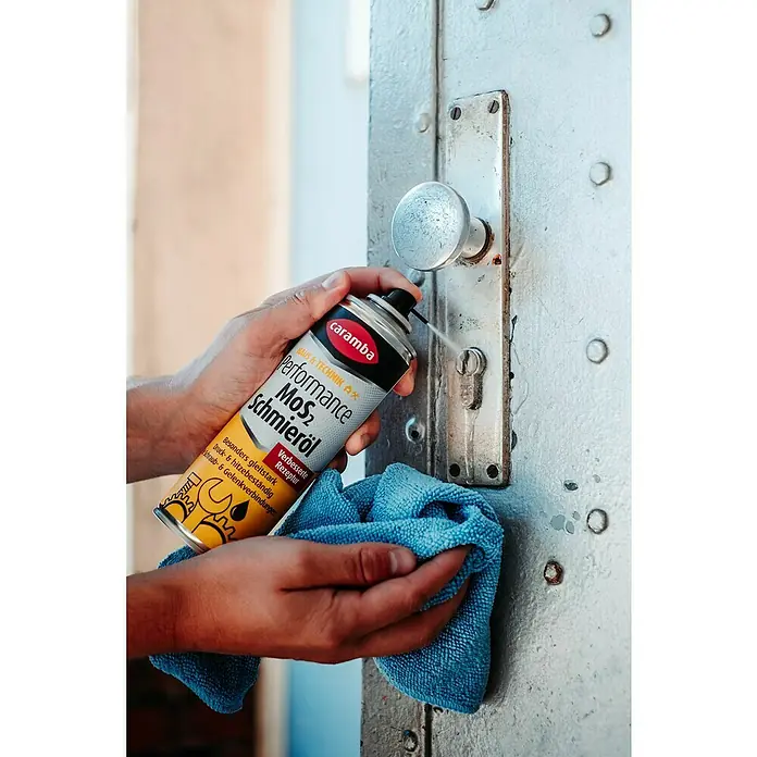Caramba Mehrzweckfett MoS2 - 300 ml - Detailaufnahme von Caramba Performance MoS2 Schmieröl, das auf ein Türschloss gesprüht wird, um die Funktionalität zu verbessern und die Lebensdauer zu verlängern.