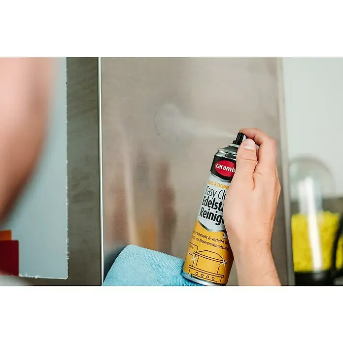 Caramba Edelstahl-Reiniger Easy Clean - 250 ml - Edelstahlreiniger im Einsatz: Eine Hand sprüht das Reinigungsmittel auf eine Edelstahlfläche, während ein Tuch bereitliegt.