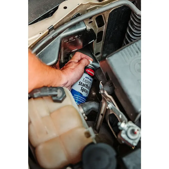 Caramba Starthilfespray Express - 300 ml - Nahaufnahme einer Hand, die eine Caramba Auto Express Starthilfe Spraydose im Motorraum eines Autos hält.