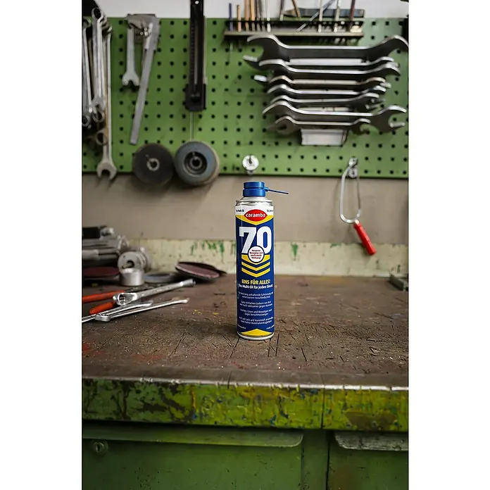 Caramba Multiöl 70 - 400 ml - Dose Caramba 70 Multifunktionsöl auf einer Werkbank mit Werkzeugen im Hintergrund.