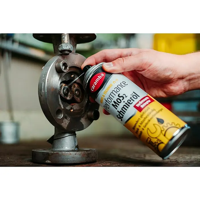 Caramba Mehrzweckfett MoS2 - 300 ml - Detailaufnahme: Eine Hand schmiert Zahnräder mit Caramba Performance MoS2 Schmieröl. Das Produkt verspricht verbesserte Schmierung und Schutz.
