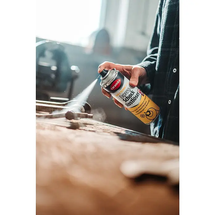 Caramba Rostlöser Express - 250 ml - Eine Hand sprüht Caramba Express Schock Rostlöser auf ein Werkstück, um es von Rost zu befreien.
