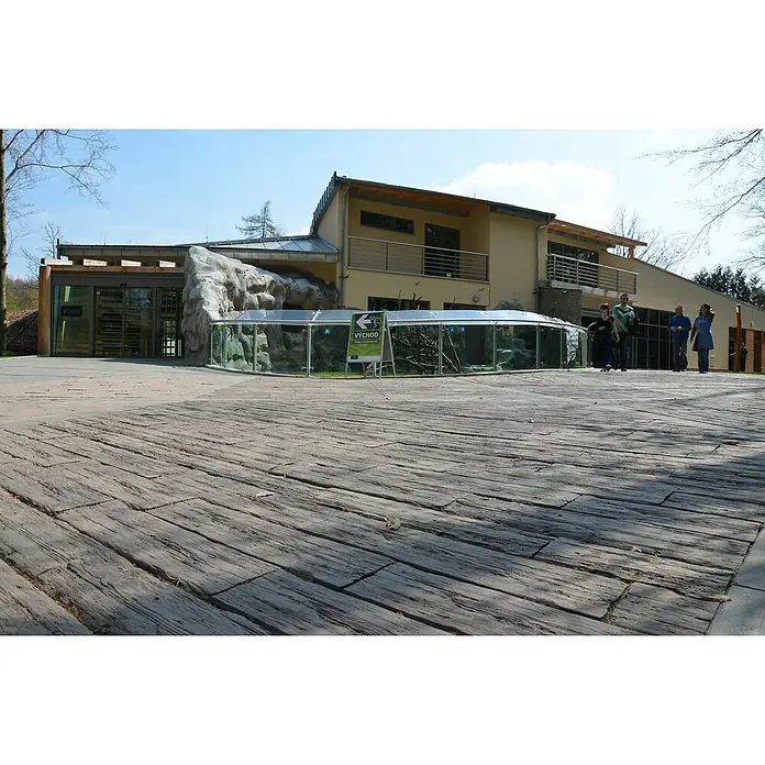 EHL Trittstein Bahnschwelle - 90 x 22,5 x 5 cm, Braun, Beton - Außenansicht eines Zoos mit Holzboden, Glasgehege und Besuchern. Das Gebäude kombiniert moderne Architektur mit natürlichen Elementen.