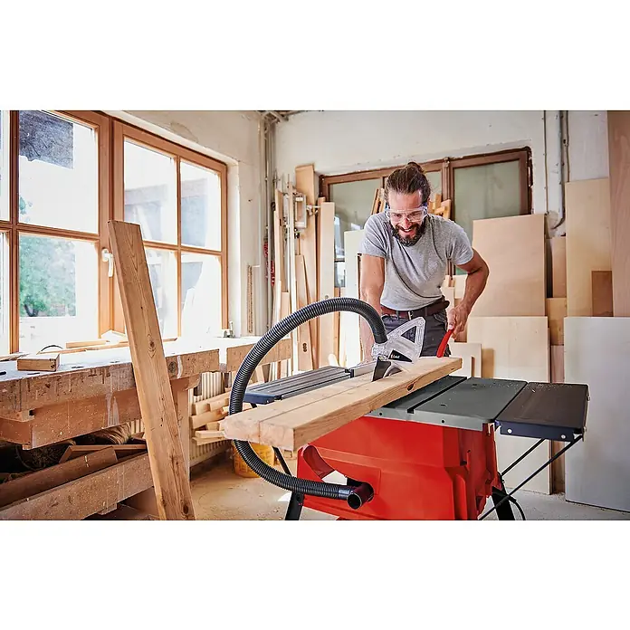 Einhell Tischkreissäge TC-TS 2025/2 U - 1.800 W, Durchmesser Sägeblatt: 250 mm, Schnitttiefe bei 90 °: 85 mm - Ein Mann, mit Schutzbrille, schneidet Holz mit einer roten Scheppach Tischkreissäge in einer Werkstatt.
