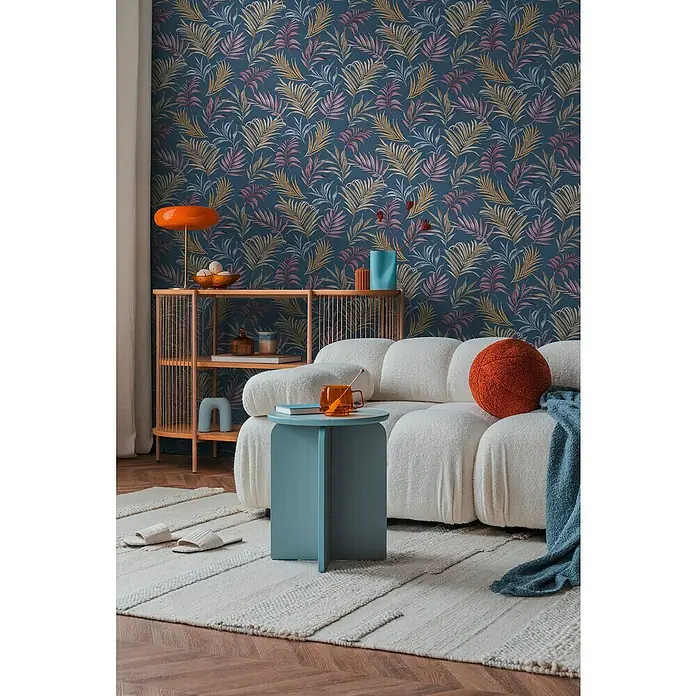 A.S. Création Cosmoliving by Cosmopolitan Vliestapete Ranken - Blau-Lila-Gelb, Floral, 10,05 x 0,53 m - Einladender Wohnraum mit einem stilvollen, weißen Sofa, einem blauen Beistelltisch und einem orangefarbenen Lampenschirm vor einer floralen Tapete.