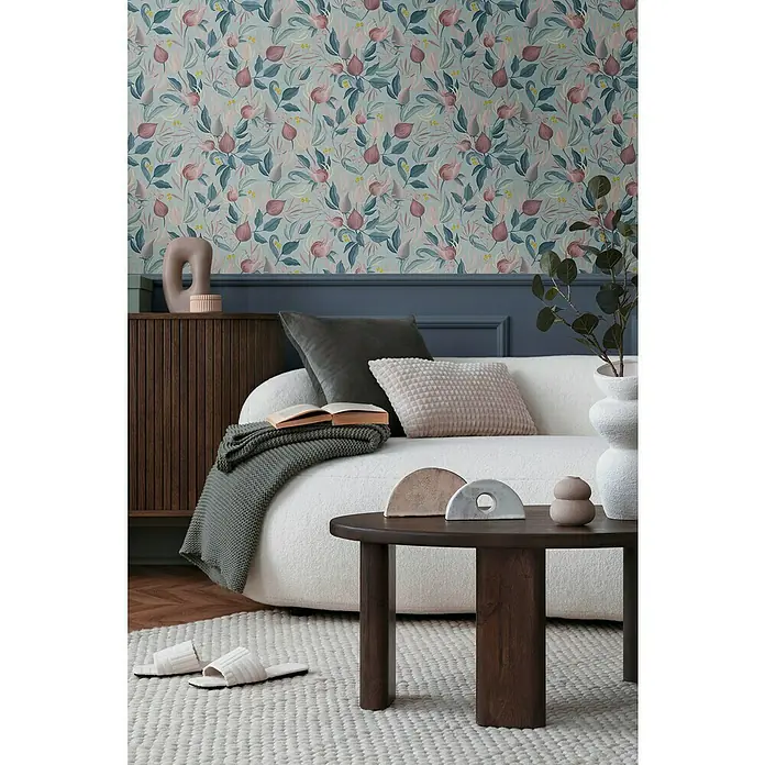 A.S. Création Cosmoliving by Cosmopolitan Vliestapete Blüte - Blau-Rosa-Pink, Floral, 10,05 x 0,53 m - Gemütliches Wohnzimmer mit floral gemusterter Tapete, Couch mit Kissen, Holztisch und Teppich mit Hausschuhen.