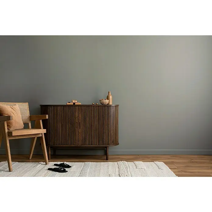swingcolor Wandfarbe Comfort Home - Ash Grey, Stumpfmatt, 1 l, Konservierungsmittelfrei - Stilvolles Interieur mit einem dunklen Holzschrank, einem hellen Holzstuhl und einem cremefarbenen Teppich auf einem warmen Holzboden.