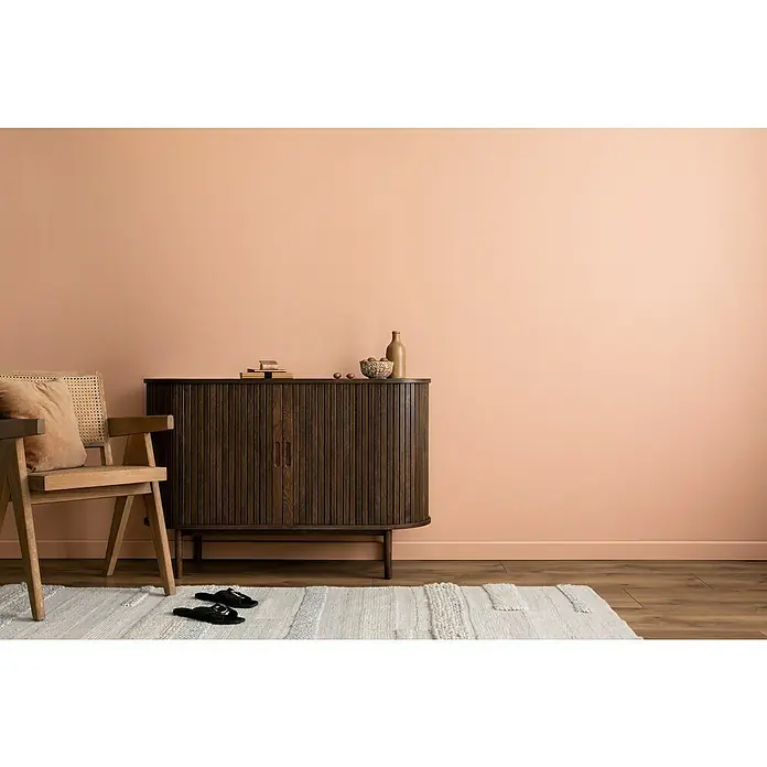 swingcolor Wandfarbe Comfort Home - Rose Rust, Stumpfmatt, 1 l, Konservierungsmittelfrei - Einladendes Wohnzimmer mit einem dunklen Holzschrank, einem hellen Holzstuhl und einem stilvollen, hellen Teppich. Die Einrichtung strahlt Wärme und Behaglichkeit aus.