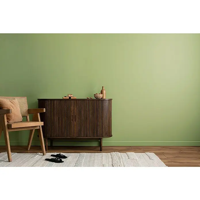 swingcolor Wandfarbe Comfort Home - Green Desire, Stumpfmatt, 2,5 l, Konservierungsmittelfrei - Einrichtungsidee mit einem dunklen Holzschrank, einem hellen Teppich und einem Holzstuhl vor einer hellgrünen Wand. Zeitloses Design für Ihr Zuhause.