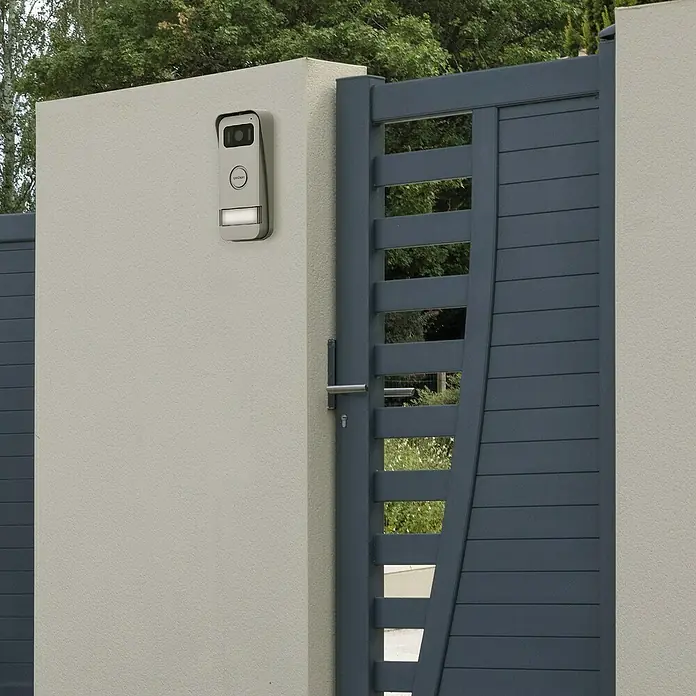 Avidsen Farb-Video-Türsprechanlage Elia Smart 2 - 1-Familienhaus - Bild einer modernen Türklingel mit Kamerafunktion an einer grauen Wand neben einem grauen Torpfosten.