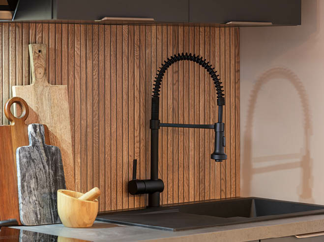 Schwarze Spüle und Armatur mit mehreren Schneidbrettern und einer Wandfliese in Holz-Optik