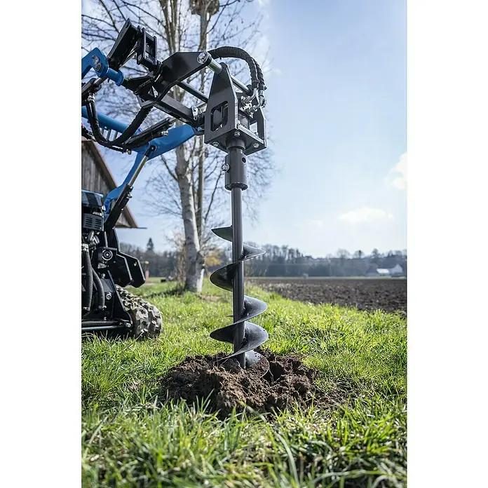 Scheppach Erdbohrer inkl. Antriebseinheit - Durchmesser: 100 cm - 200 cm, Passend für: Scheppach Kompaktlader MKL730 - Bodenbearbeitungsgerät im Einsatz auf einem Feld. Der Erdbohrer ist an einem Traktor befestigt und dient zum Ausheben von Löchern.