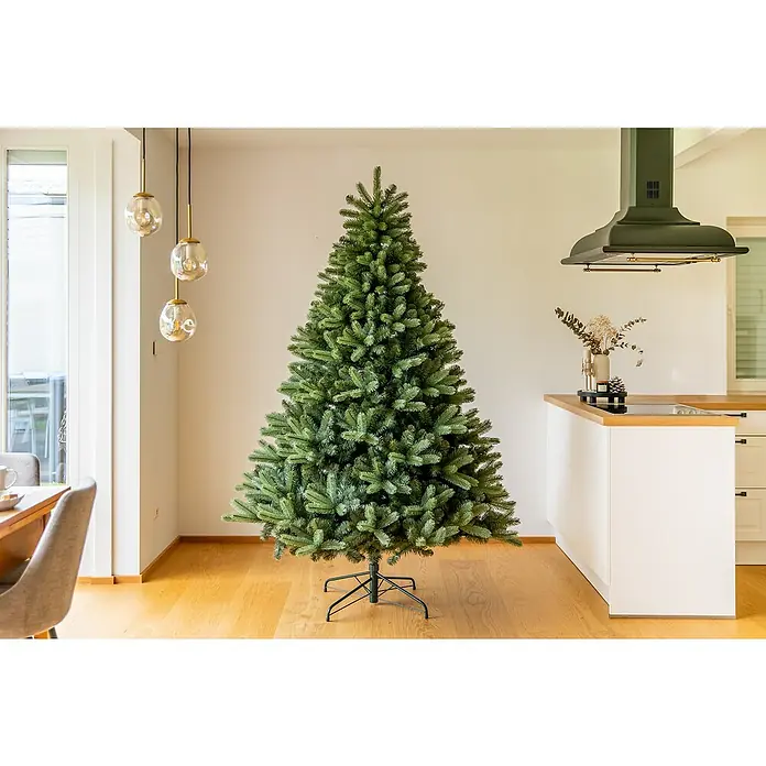 50 NRTH Künstlicher Weihnachtsbaum Vermont - Höhe: 210 cm, Grün, Standfuß - Ein ungeschmückter, üppiger Weihnachtsbaum steht auf einem Holzboden in einem hellen Raum und verbreitet festliche Stimmung.
