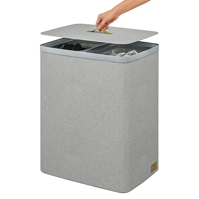 Store It Premium Wäschesammler Ava - 67 x 56 x 40 cm, Grau - Grauer Wäschekorb mit zwei Fächern und Deckel. Eine Hand öffnet den Deckel des modernen, rechteckigen Wäschebehälters.