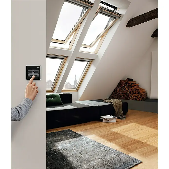 Velux Elektro-Schwingfenster GGL MK04 307021 Thermo - 78 x 98 cm - Intelligente Haussteuerung: Eine Hand bedient ein smartes Bedienfeld zur Steuerung der Dachfenster in einem modernen Dachzimmer.