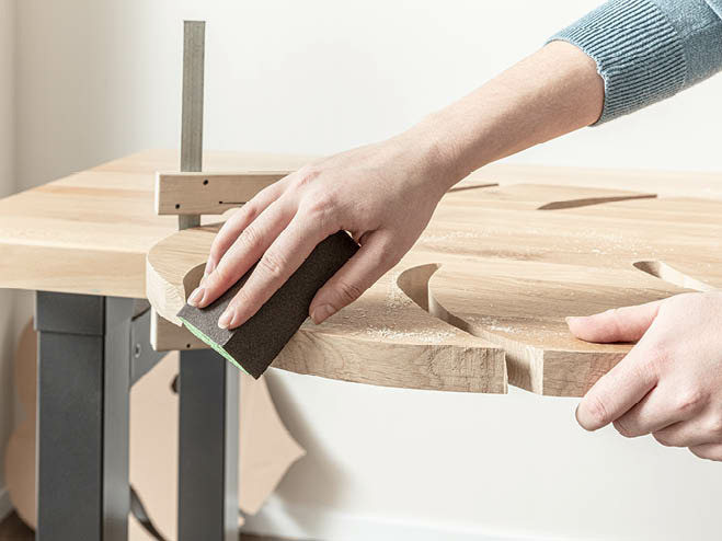 Die Kanten vom Holzbrett in Monstera-Blatt Form werden mit einem Schleifschwamm glatt gemacht