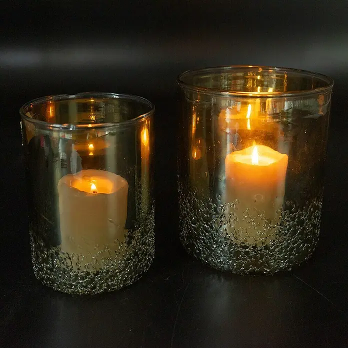 Windlicht Verde - Ø x H: 10 x 13 cm, Grün - Stimmungsvolle Aufnahme von zwei goldenen Kerzenhaltern mit jeweils einer brennenden Kerze, die warmes Licht spenden.