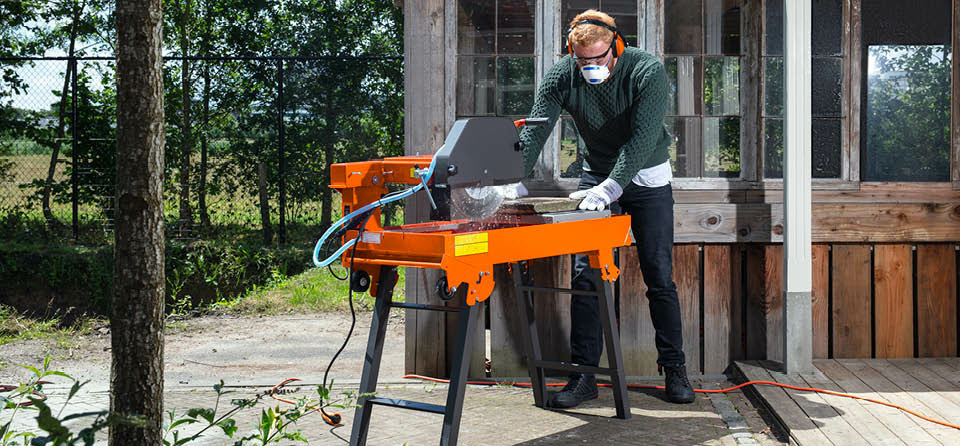 Mann bedient die Boels Steintrennmaschine im Garten mit passendem Arbeitsschutz
