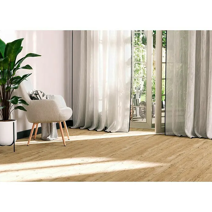 Feinsteinzeugfliese Essenza - 30 x 120 cm, Caldo, Matt - Ein helles Zimmer mit einem eleganten Sessel, einer grünen Pflanze und einem schönen Holzboden, der dem Raum Wärme verleiht. Helle Vorhänge sorgen für Ambiente.