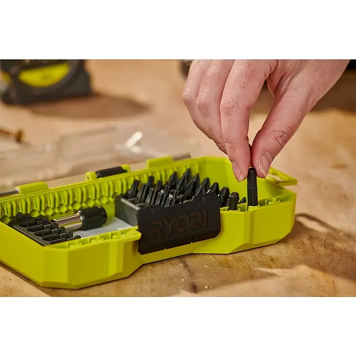 Ryobi Bit-Set RARXSD31 - Bitlänge: 25 mm, 31 -tlg. - Nahaufnahme eines Ryobi-Bit-Sets, bei dem eine Hand einen Bit entnimmt. Das Set ist gelb und enthält verschiedene Schrauberbits.