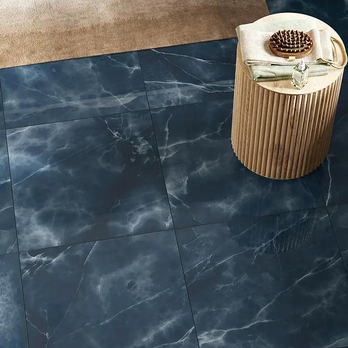 Atlas Concorde Solution Marble Vison Feinsteinzeugfliese Onice Blue - 60 x 60 cm, Blau, Glänzend - Ansicht von oben: Eine quadratische, blaue Marmorfliese sorgt für einen eleganten Look im Badezimmer, ergänzt durch einen Beistelltisch und Badaccessoires.