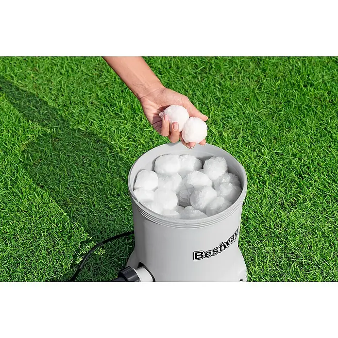 Bestway Filterpumpe - Ø x H: 27,2 x 42,1 cm, Filterleistung: 5.678 l/h - Eine Hand fügt Bestway Flowclear Polysphere Filterbälle in einen Filterbehälter auf Rasen hinzu.