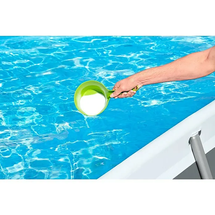 Bestway Salzwassersystem Hydrogenic - Passend für: Filtersysteme ab 1.249 l/h Leistung, Benötigte Start-Salzmenge: 3 g/l - Eine Person gibt mit einer grünen Schöpfkelle Poolchemikalien in ein Schwimmbad, um das Wasser sauber und klar zu halten.