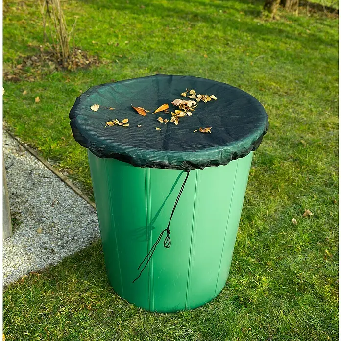 Windhager Laubschutznetz - Schwarz, Durchmesser: 95 cm - Ein grüner Kompostbehälter mit schwarzem Netzdeckel steht auf einer Rasenfläche, bedeckt mit einigen Herbstblättern.