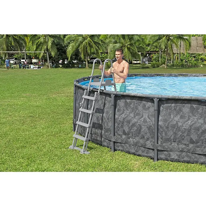 Bestway Frame-Pool Set APX365 - Ø x H: 671 x 132 cm, Dunkler Marmor, 40.377 l - Ein Mann steigt mit einer grauen Leiter in einen Pool im Freien. Die Leiter erleichtert den Zugang zu dem Pool.
